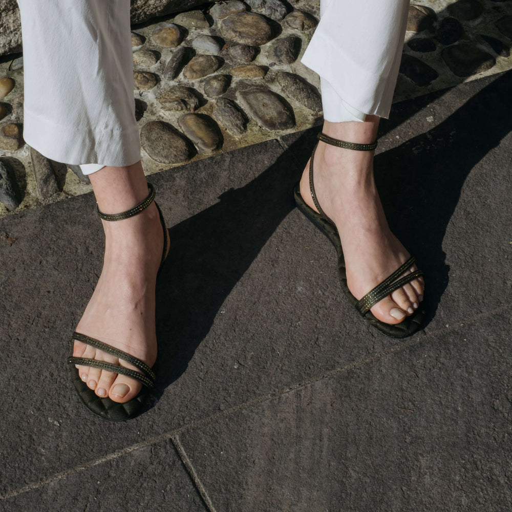 Woman wearing AERA FAYE Military Crystal Sandals with crystal straps and buckle-fastening ankle detail. Vegan, designer, and sustainable shoes.